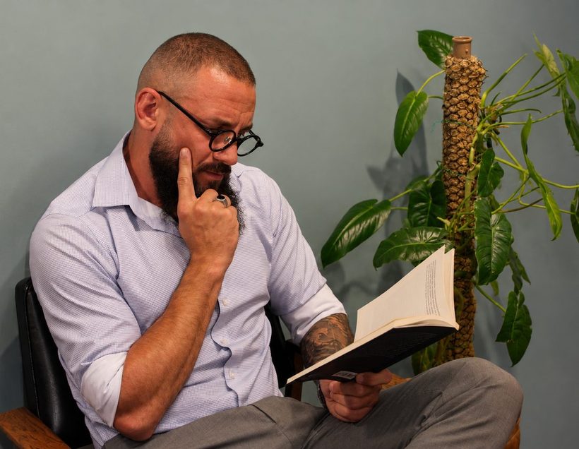 Lucas Coutinho lendo um livro no consultório, ao lado de uma planta.